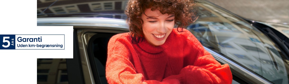 Smilende kvinde hænger ud af vinduet på Hyundai i30 5-dørs med "5-års garanti" logo henover 