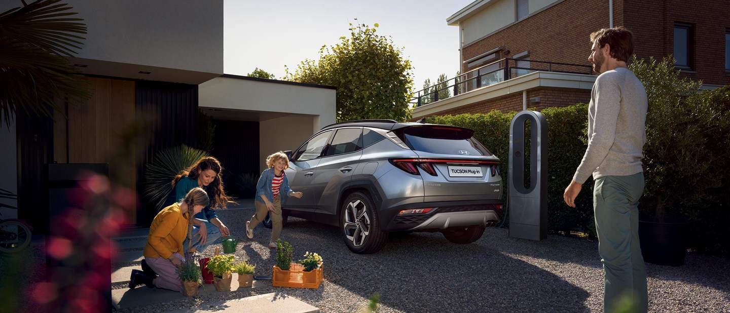 Hyundai TUCSON Plug-in Hybrid parkeret i indkørsel mens familie kigger på planter