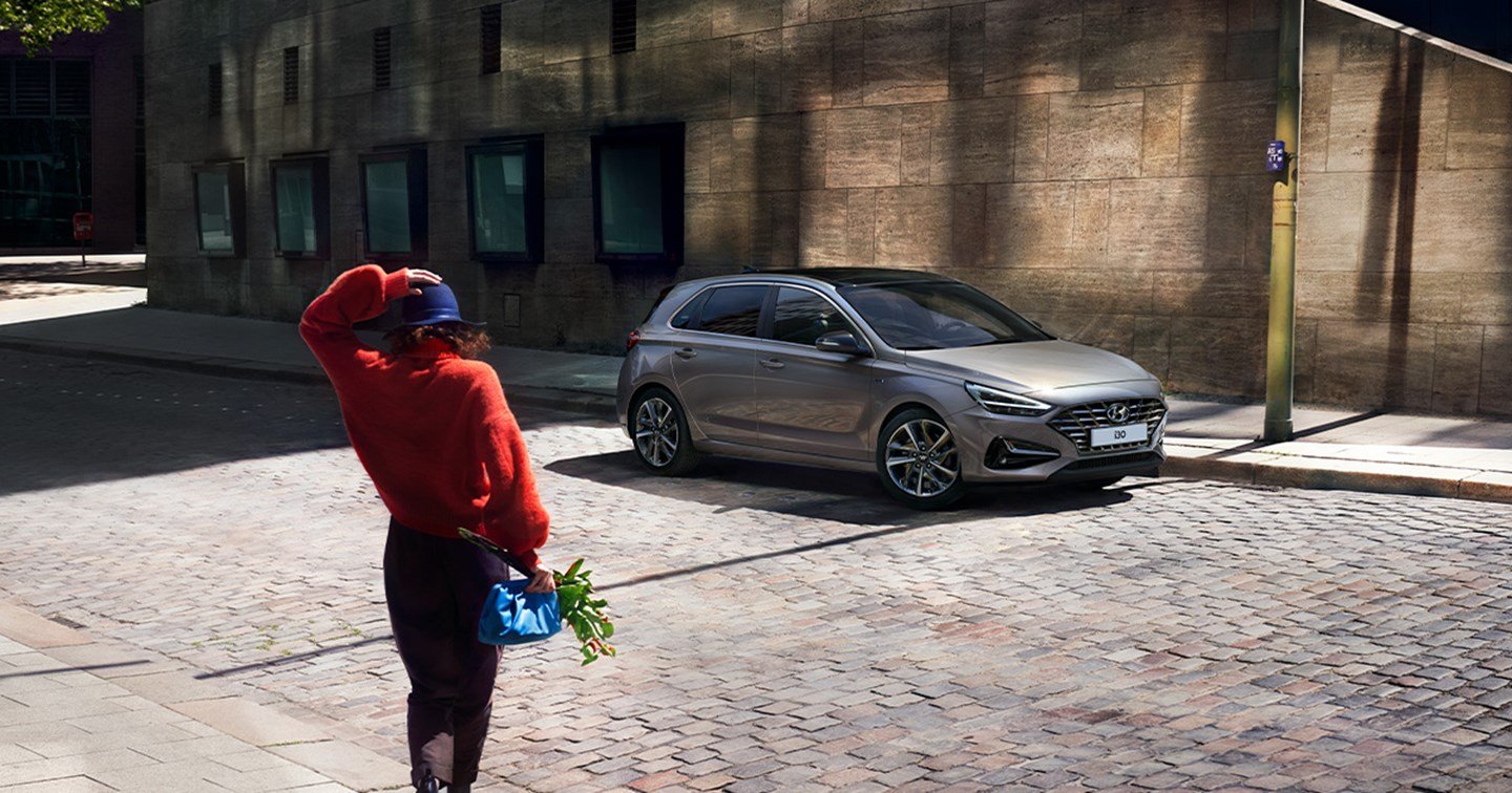 Kvinde med blomster går mod en parkeret Hyundai i30 5-dørs