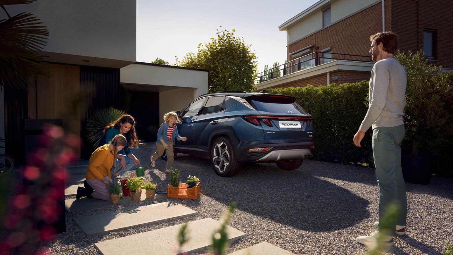 Børnefamilie planter blomster og leger ved siden af Hyundai TUCSON Plug-in Hybrid parkeret i indkørslen 