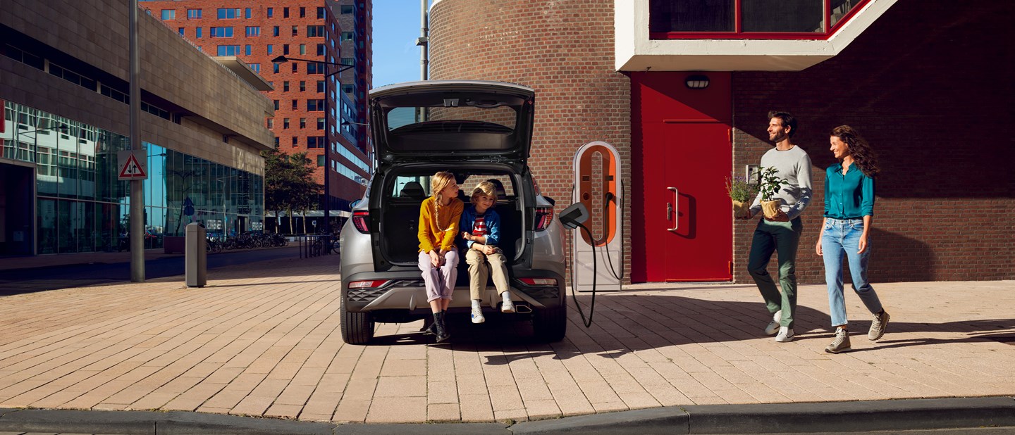 Forældre gående mod børn i åben bagagerum på Hyundai TUCSON Plug-in Hybrid der oplades 
