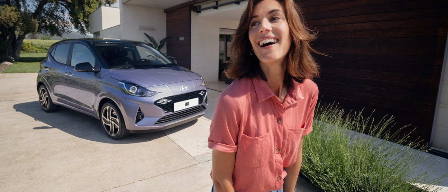 Smilende kvindelig Hyundai-ejer foran sin Hyundai i10 