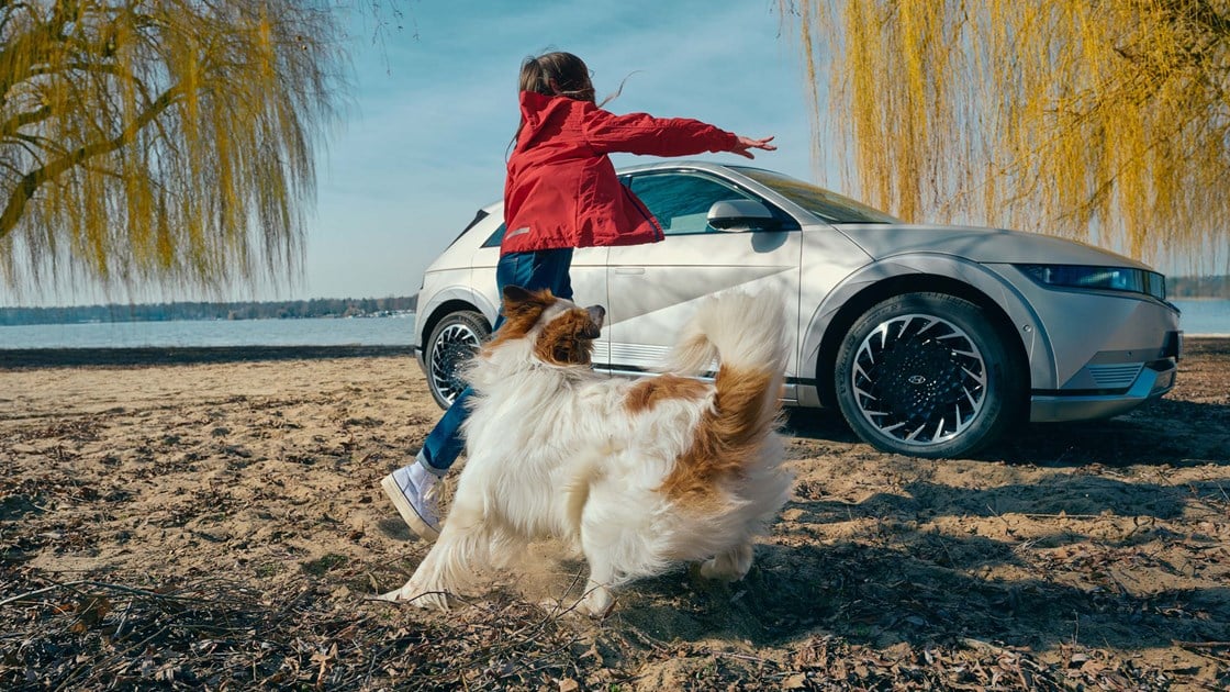 Pige leger med hund på strand foran parkeret Hyundai IONIQ 5