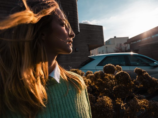 Kvinde med sol i ansigtet og vind i håret med parkeret IONIQ 5 i baggrunden 