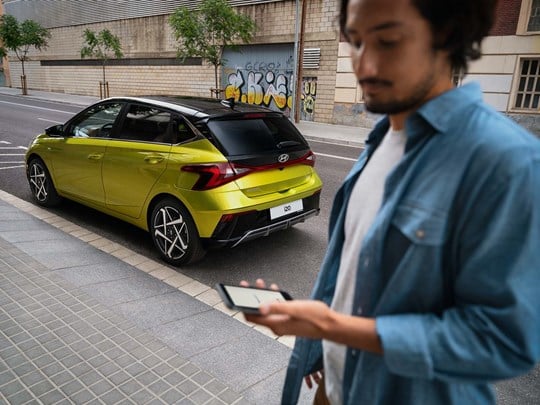 Mand står med smartphone foran parkeret Hyundai i20
